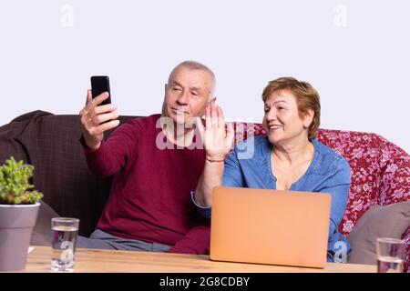 Mann und Frau sitzen vor dem Computer mit zwei Gläsern Wasser am Tisch und unterhalten sich online auf dem Handy. Stockfoto