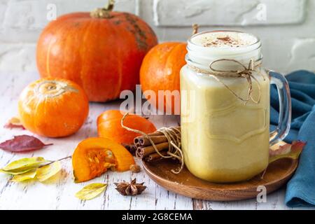 Herbstgetränk. Kürbis gewürzter Latte oder Kaffee im Glas auf einem rustikalen Holztisch. Stockfoto