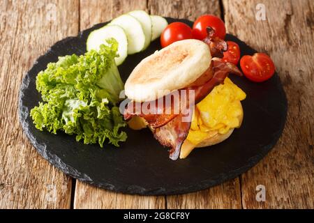 Hausgemachtes Frühstücksei-Sandwich mit Käsespeck auf einem englischen Muffin auf einem Schieferbrett auf dem Tisch. Horizontal Stockfoto