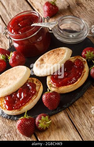 Englische Muffins mit Erdbeermarmelade aus der Nähe auf dem Tisch, rustikaler Stil. Vertikal Stockfoto