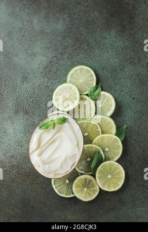 Glas mit kosmetischem Produkt mit Kalk- und Minzhälften auf grünem Beton. Natürliche Zitruskosmetik mit Vitamin C. Copy Space. Stockfoto