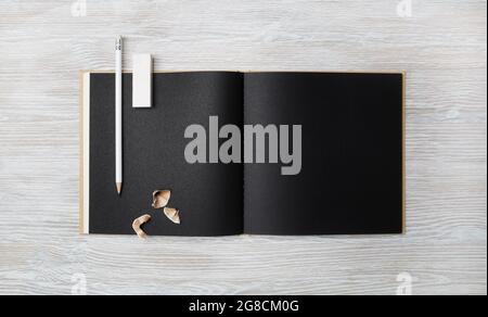 Unbeschriftete schwarze Broschüre, Bleistift und Radierer auf hellem Holzhintergrund. Branding-Modell. Flach liegend. Stockfoto