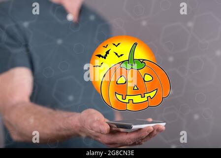 Halloween-Konzept über einem Smartphone von einem Mann im Hintergrund gehalten Stockfoto