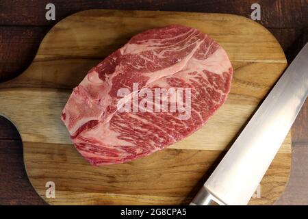 Short Rib oder Costela Premium. Schönes rohes Steak unter einem Holzbrett auf einem Holzhintergrund. Für einen brasilianischen Grill. Stockfoto