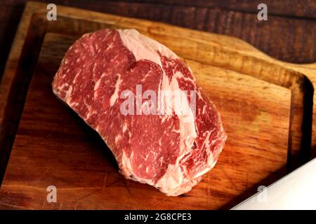 Short Rib oder Costela Premium. Schönes rohes Steak unter einem Holzbrett auf einem Holzhintergrund. Für einen brasilianischen Grill. Stockfoto
