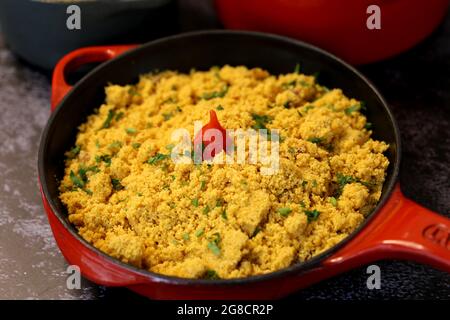 Roter Eisentopf mit Farofa. Traditionelle brasilianische Küche. Auf einem dunklen Hintergrund. Stockfoto