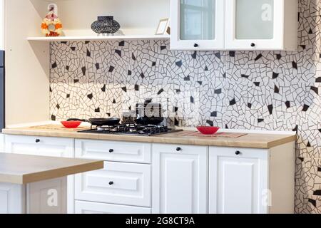 Neue moderne Wohnküche mit Holztisch und Herd mit Pfannen auf Keramikfliesen im Hintergrund. Stockfoto