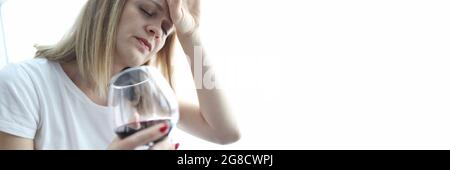 Müde Frau mit einem Glas Rotwein hält ihren Kopf Stockfoto