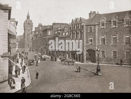 Ein Blick aus dem späten 19. Jahrhundert auf die High Street in Hawick, einer Stadt an der schottischen Grenze und der historischen Grafschaft Roxburghshire im östlichen südlichen Hochland. Am Ende der Straße befindet sich das markante Rathaus im schottisch-baronialen Stil von Hawick mit seinen vielen Sandsteingebäuden mit Schieferdächern. Stockfoto