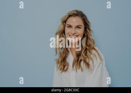 Fröhliche blonde Frau, die im Studio steht und mit einem breiten Lächeln millt Stockfoto