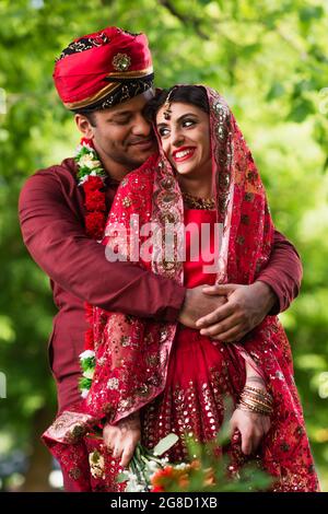 Glücklicher indischer Mann im Turban umarmt Braut in rotem Sari Stockfoto