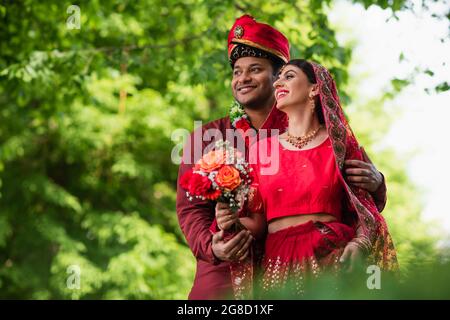 Fröhlicher indischer Mann im Turban umarmt Braut in rotem Sari Stockfoto