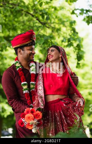 Positiver indischer Mann im Turban umarmt Braut in rotem Sari Stockfoto
