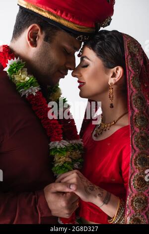 Seitenansicht eines lächelnden indischen Ehemannes und seiner Frau in traditioneller Kleidung mit isolierten Händen auf Weiß Stockfoto