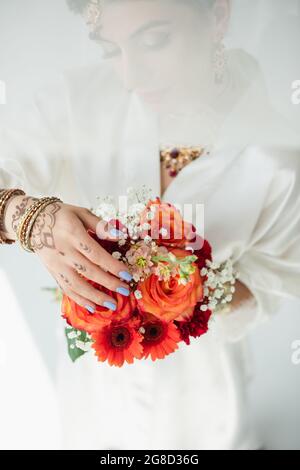 Junge indische Braut mit Mehndi, die Blumen auf Weiß hält Stockfoto