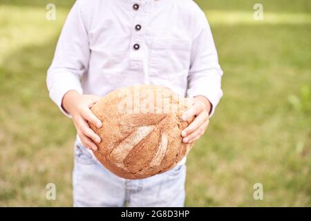 Das Kind hält ein rundes Brot. Gesunde Ernährung. Großes frisches Bäckerbrötchen tragen Stockfoto