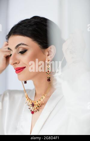 Glückliche junge indische Braut trägt Halskette auf weiß Stockfoto