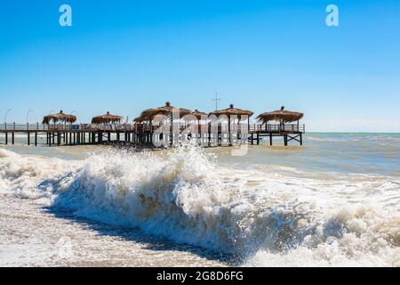 Strandpalmenhütten auf Holzdock in einem welligen Meer. Konzept für das Ende der Sommersaison. Stockfoto