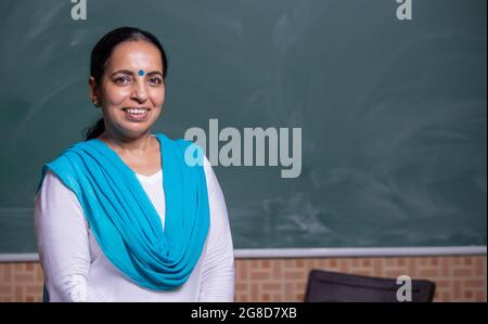Porträt eines selbstbewussten indischen Lehrers, der vor der schwarzen Tafel im Klassenraum steht Stockfoto