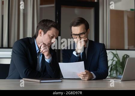 Zwei seriöse Geschäftsleute, fokussierte Geschäftspartner, Mitarbeiter beim Lesen des Dokuments Stockfoto