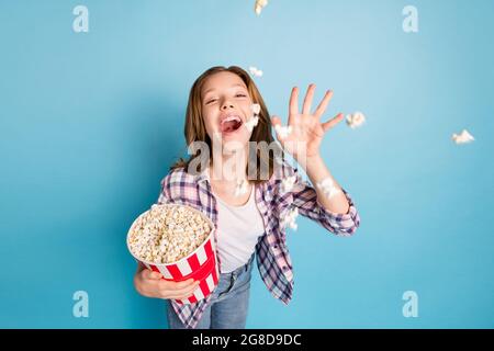 Foto von optimistischen roten Frisur Mädchen essen Pop Mais tragen Hemd Jeans isoliert auf blauem Hintergrund Stockfoto