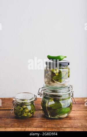 Drei Glas Jalapeno Peppers aus der frischen Dose mit Kräutern und Knoblauch auf einem Holztisch. Speicherplatz Kopieren Stockfoto