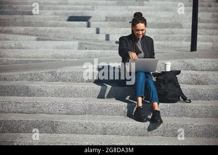 Lächelnder, zufriedener Freiberufler, der auf den konkreten Stufen sitzt Stockfoto