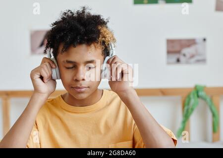 Porträt eines Teenagers mit gemischten Rassen, der Kopfhörer trägt und Musik mit geschlossenen Augen hört, Kopierraum Stockfoto