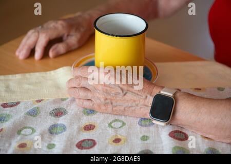 Ältere Frau mit moderner Smart Watch trinkt Morgenkaffee. Intelligente Uhr mit leerem schwarzen Bildschirm, Platz für Ihr Design. Gesundheitswesen und Technologie Co Stockfoto