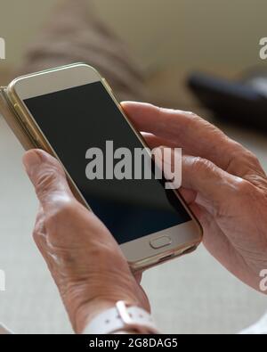Die Hände einer älteren Frau halten ein Smartphone mit leerem Bildschirm. Nahaufnahme. Speicherplatz kopieren, Mockup. Stockfoto