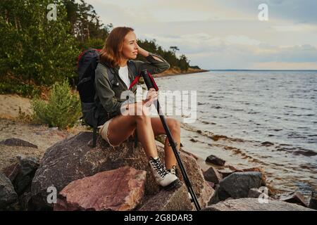 Wanderer machen einen Halt und ruhen sich auf einem Felsen in der Nähe des Sees aus Stockfoto