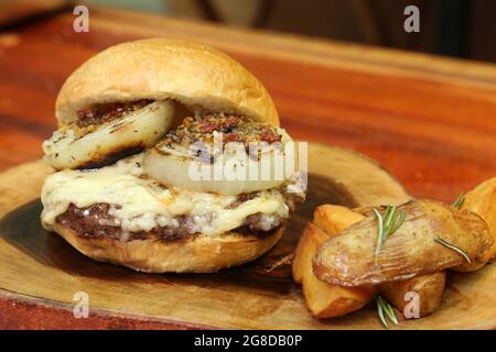 Burger mit Zwiebel auf der Oberseite und Chimichurri. Auf einem rustikalen Holzhintergrund. Stockfoto