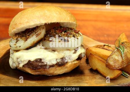 Burger mit Zwiebel auf der Oberseite und Chimichurri. Auf einem rustikalen Holzhintergrund. Stockfoto