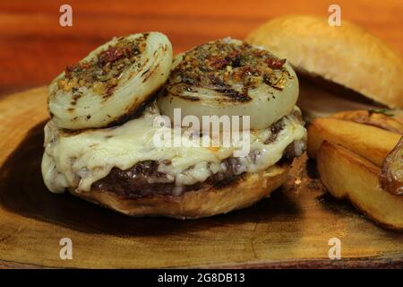 Burger mit Zwiebel auf der Oberseite und Chimichurri. Auf einem rustikalen Holzhintergrund. Stockfoto