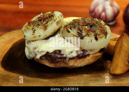 Burger mit Zwiebel auf der Oberseite und Chimichurri. Auf einem rustikalen Holzhintergrund. Stockfoto