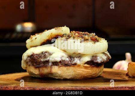 Burger mit Zwiebel auf der Oberseite und Chimichurri. Auf einem rustikalen Holzhintergrund. Stockfoto