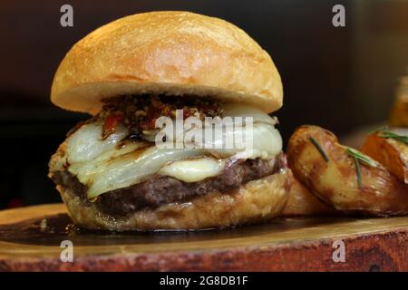 Burger mit Zwiebel auf der Oberseite und Chimichurri. Auf einem rustikalen Holzhintergrund. Stockfoto
