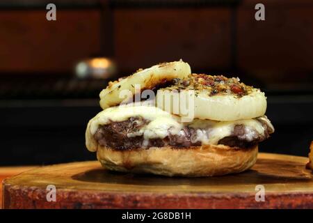 Burger mit Zwiebel auf der Oberseite und Chimichurri. Auf einem rustikalen Holzhintergrund. Stockfoto