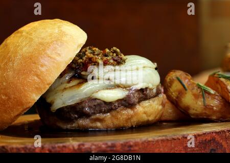 Burger mit Zwiebel auf der Oberseite und Chimichurri. Auf einem rustikalen Holzhintergrund. Stockfoto