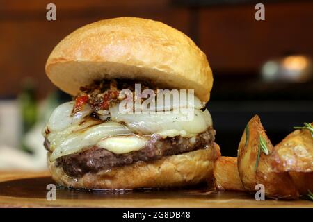 Burger mit Zwiebel auf der Oberseite und Chimichurri. Auf einem rustikalen Holzhintergrund. Stockfoto
