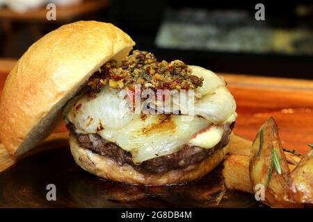 Burger mit Zwiebel auf der Oberseite und Chimichurri. Auf einem rustikalen Holzhintergrund. Stockfoto