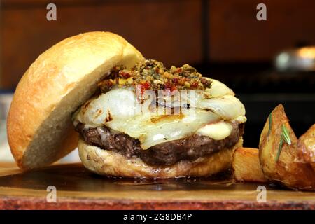 Burger mit Zwiebel auf der Oberseite und Chimichurri. Auf einem rustikalen Holzhintergrund. Stockfoto