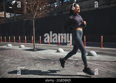 Fröhliche, gut aussehende Sportlerin, die morgens mit aktivem Joggen gekleidet ist Stockfoto