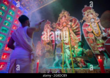 Verschwommenes Bild eines hinduistisch-bengalischen Priesters, der die Göttin Durga mit Schari anbetet, indisches Frauenkleid, während Durga Puja unter heiligem Rauch. Aufgenommen unter Farben Stockfoto