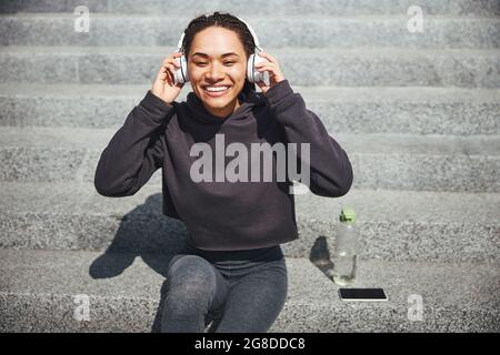 Frau mit einem fröhlichen Lächeln auf den Betontreppen sitzend Stockfoto