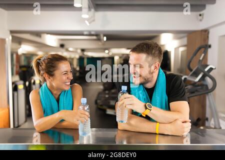 Ein glückliches Paar mit Handtüchern und Wasserflaschen, während man sich in einem Fitnessclub ausruhte Stockfoto