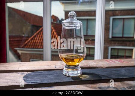 DRAM von Single Malt Scotch Whisky serviert in Probierglas mit Blick auf alte Fenster und Häuser auf gebrauchte Holzkiste Stockfoto