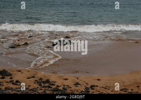 Kleine Wellen Rollen auf einen hellbraunen Sandstrand mit vulkanischem Gestein an der Maalaea Bay in Kihei, Maui, Hawaii, USA Stockfoto