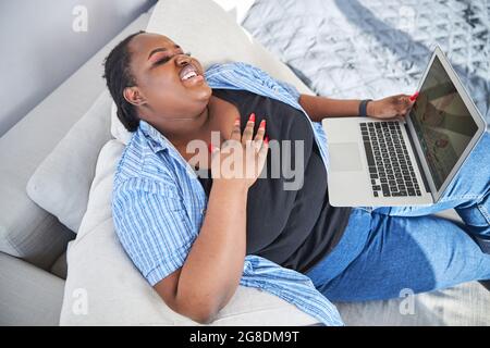 Fröhliche afroamerikanische Dame, die Unterhaltung im Internet genießt Stockfoto