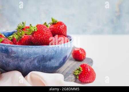 Reife Erdbeeren in blauer Schale auf rustikalem Holzbrett, eleganter Stil, süße Beere als Sommerdessert. Gefüllte Schüssel oder Teller mit roten frischen Erdbeeren. Stockfoto